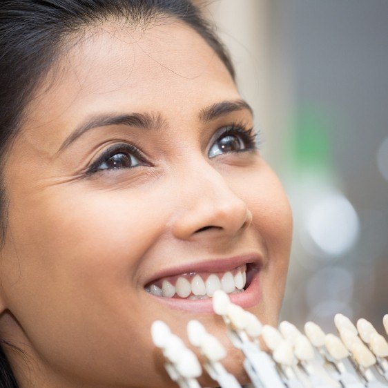 Woman's smile compared with porcelain veneer color chart during cosmetic dentistry visit