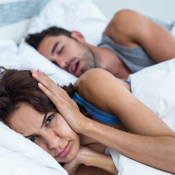 Frustrated woman in bed next to snoring man in need of slee apnea therapy